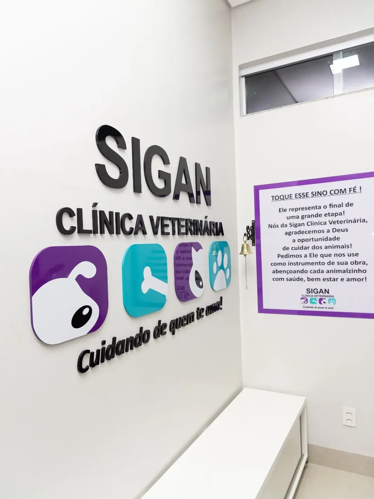 Parede da Sigan com o sino e o cartaz Toque esse sino com fé